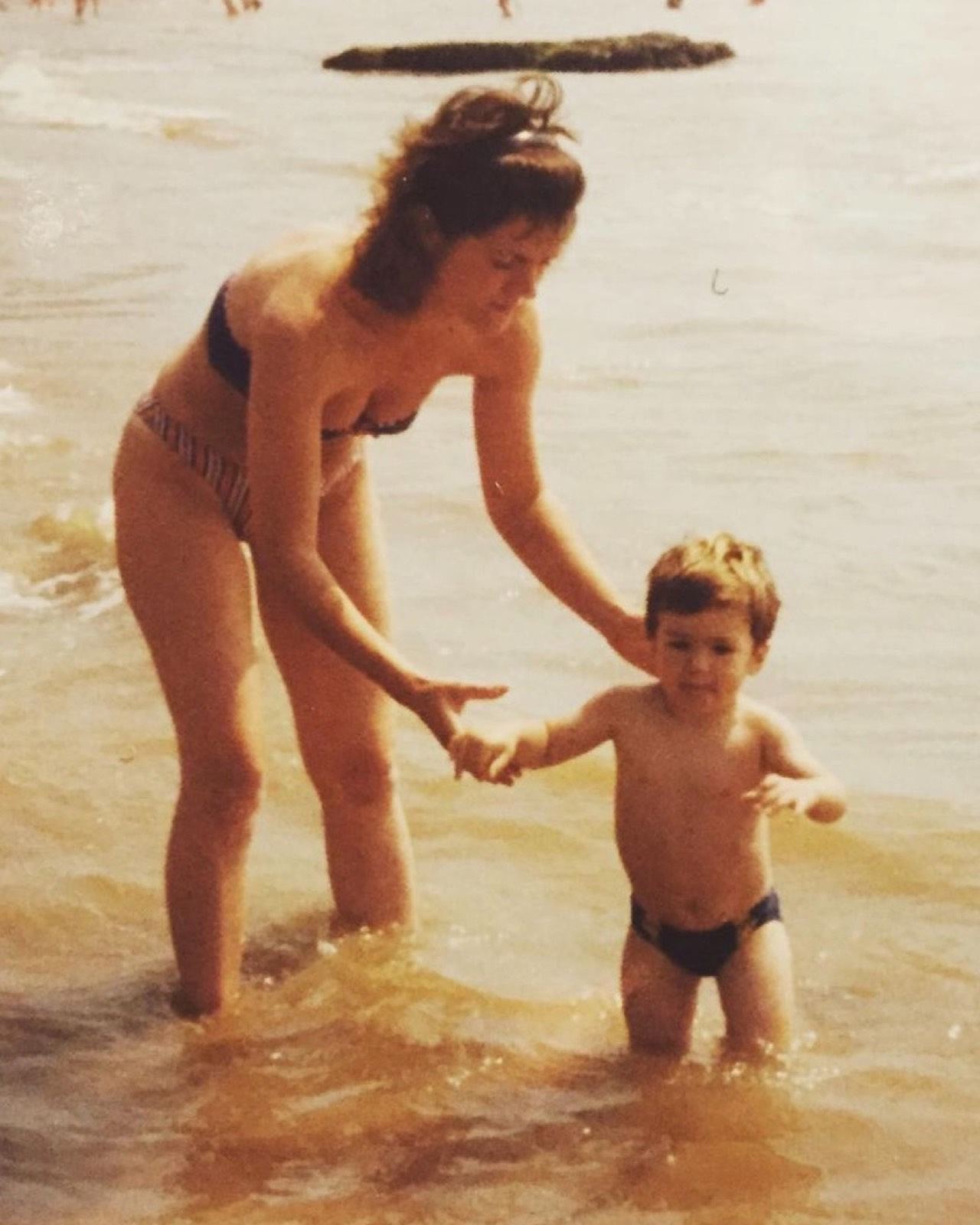 James as a small boy, holding his mother's hands in the shallows at the beach