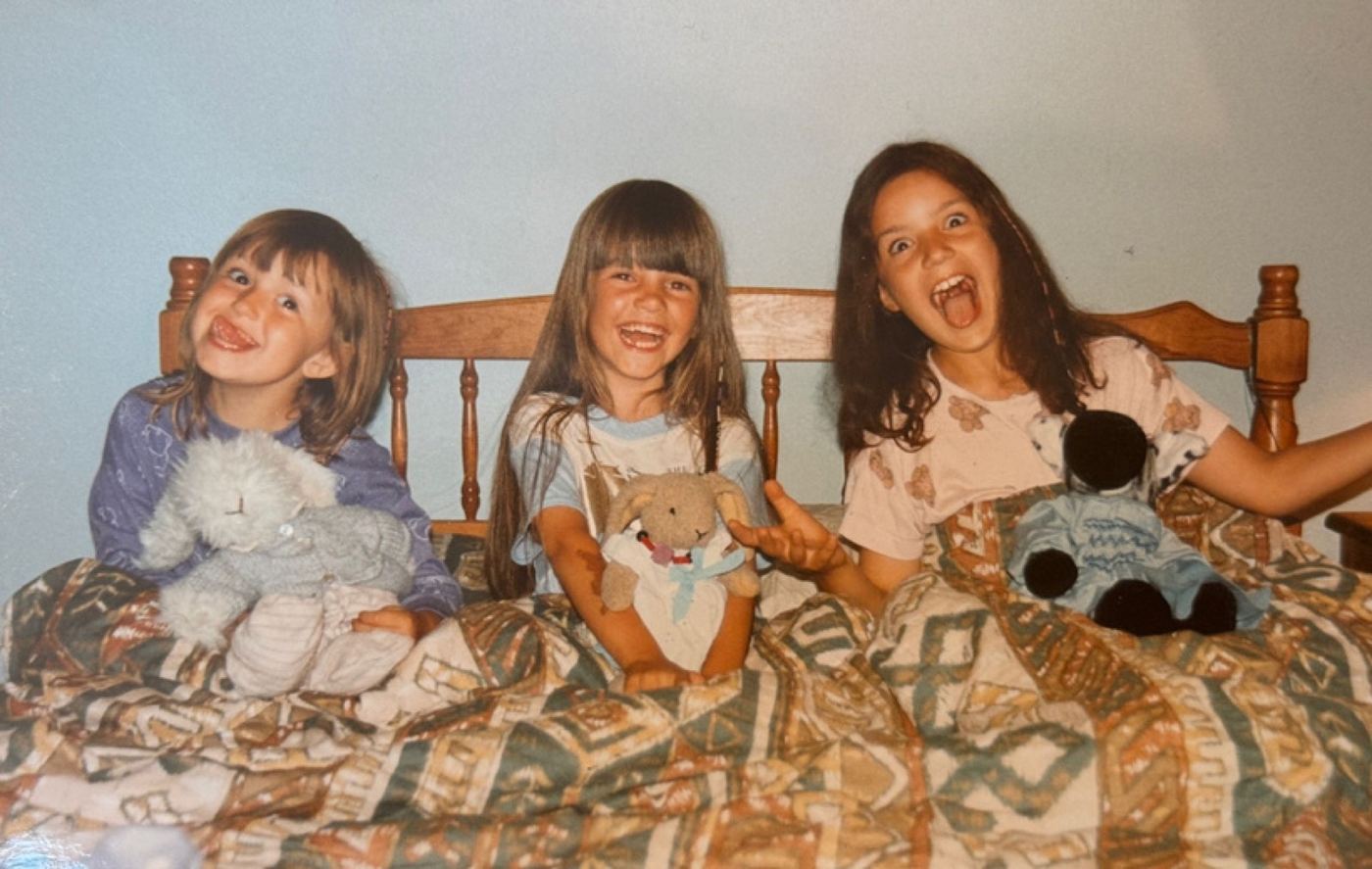 Three young children laughing together in bed with their soft toys