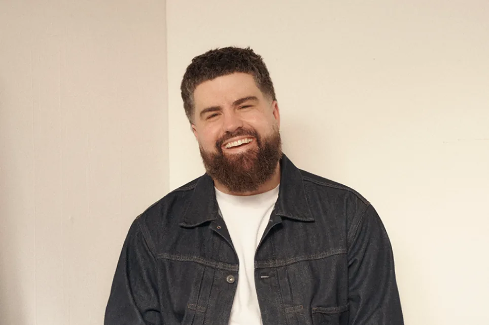 James laughing, in a denim jacket against a plain wall