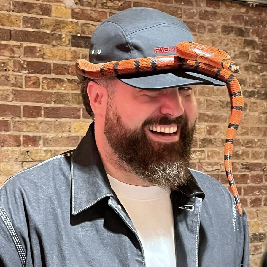James laughing in a cap, with a snake resting on the brim